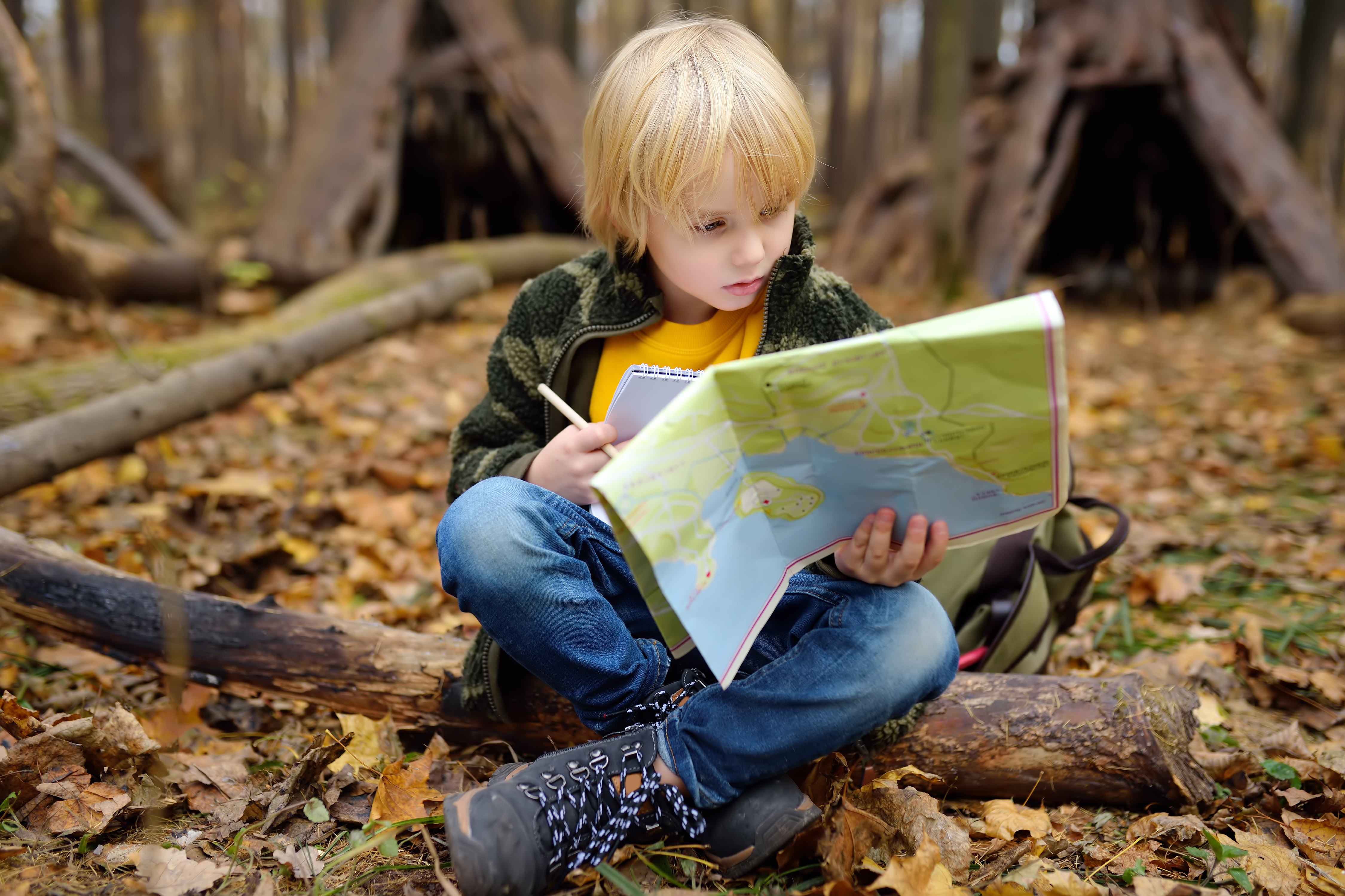 Young boy sitting in a wood reading a map