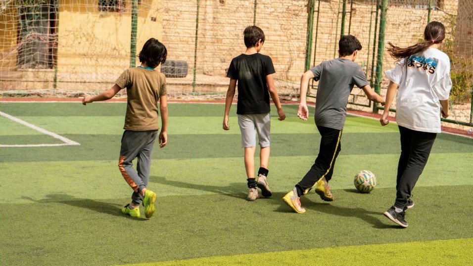 Four children with their backs to the camera playing football at a youth or sports club