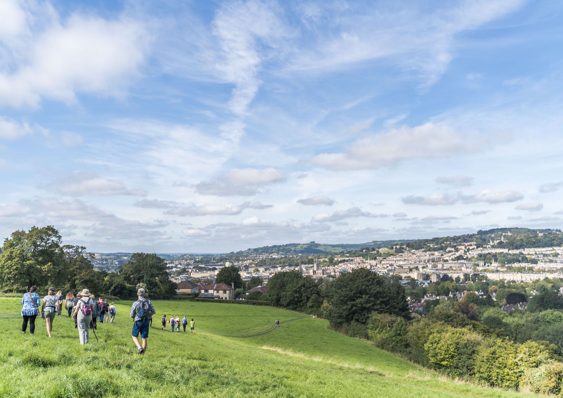 A group of walkers on a green hillside with views across a city and a bright blue skyline