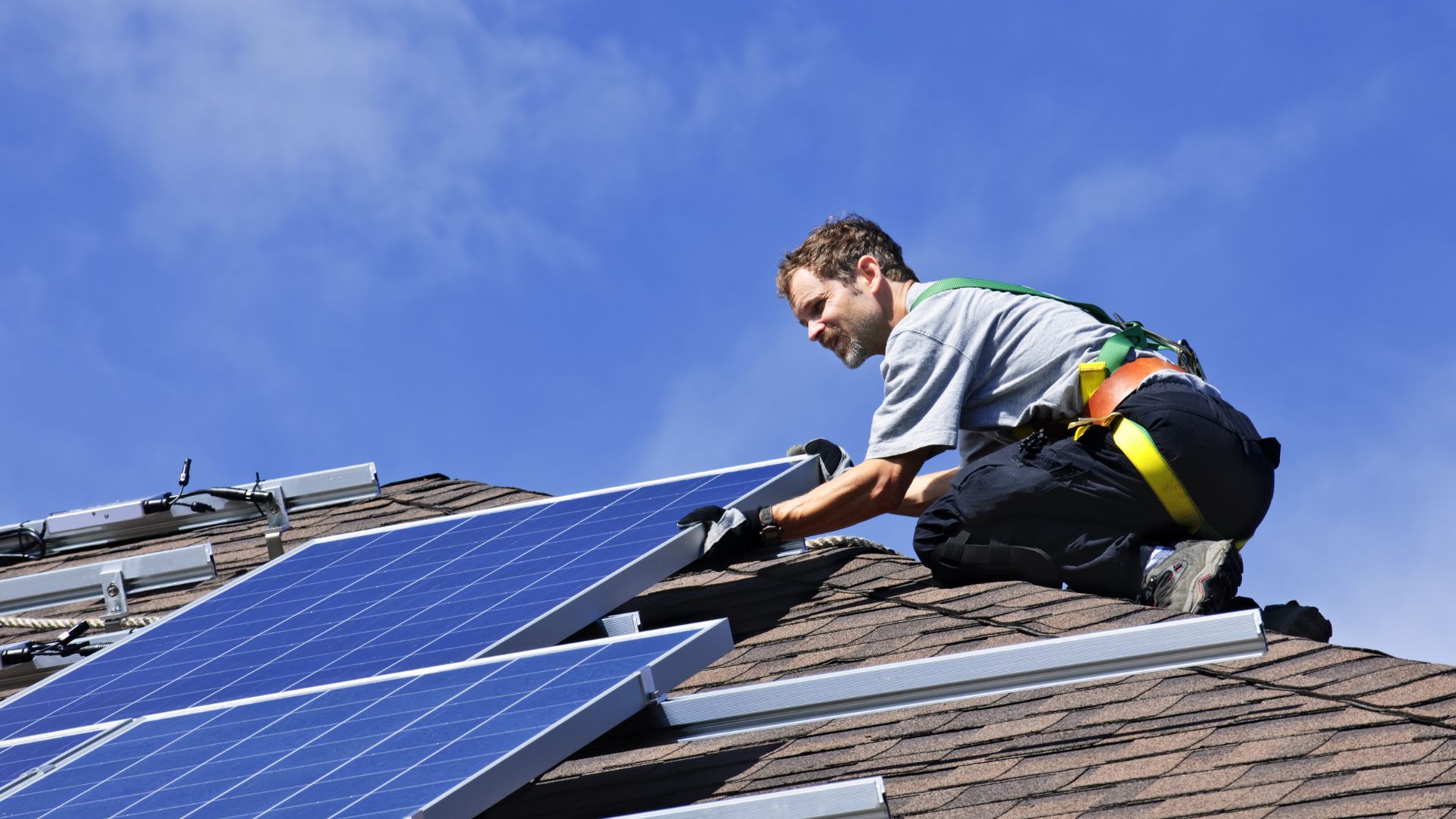 Man on a roof fixing solar panels in bright sunshine