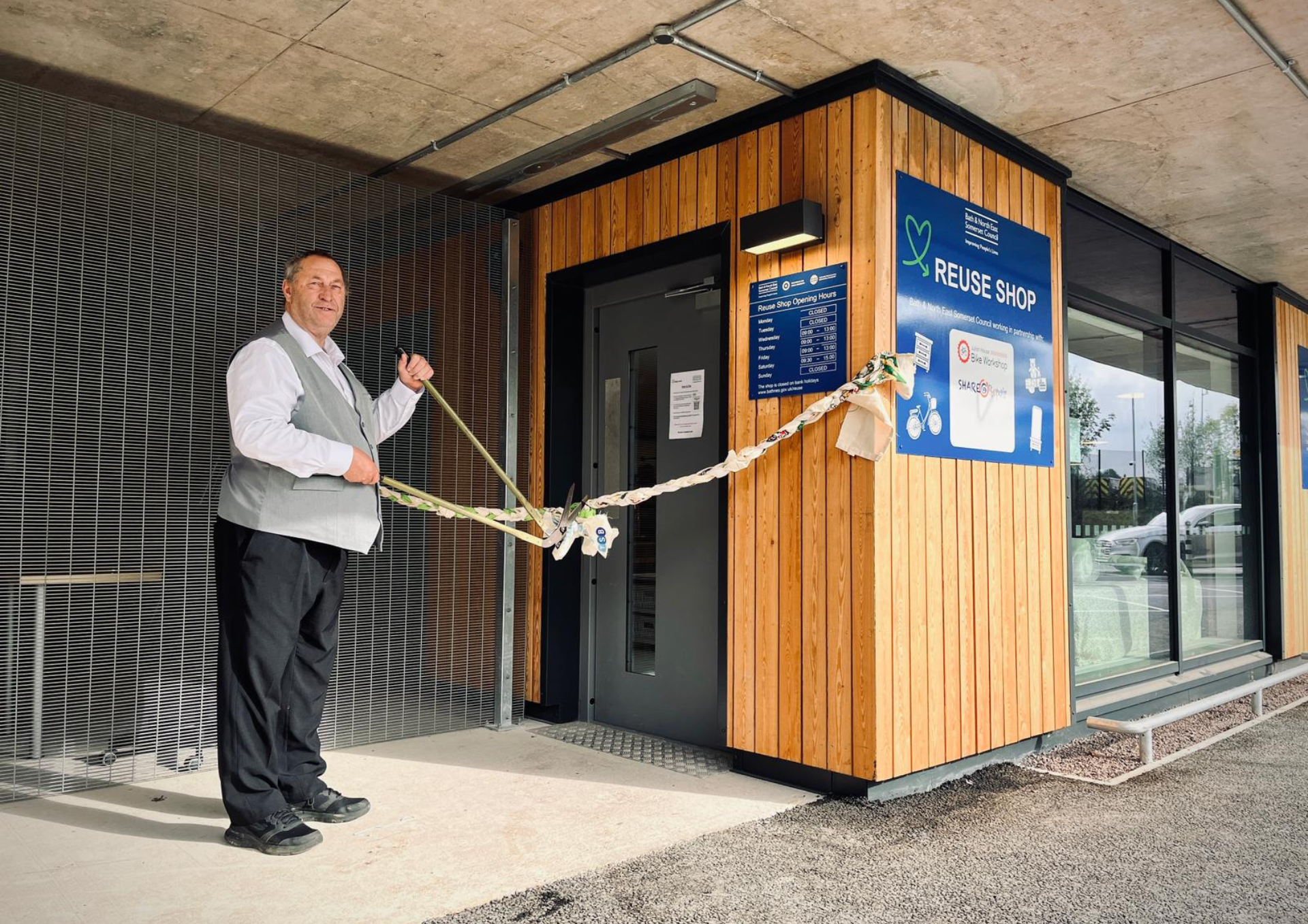 Man outside the entrance to a building cutting a 'ribbon' made of hessian sacks with a pair of gardening shears