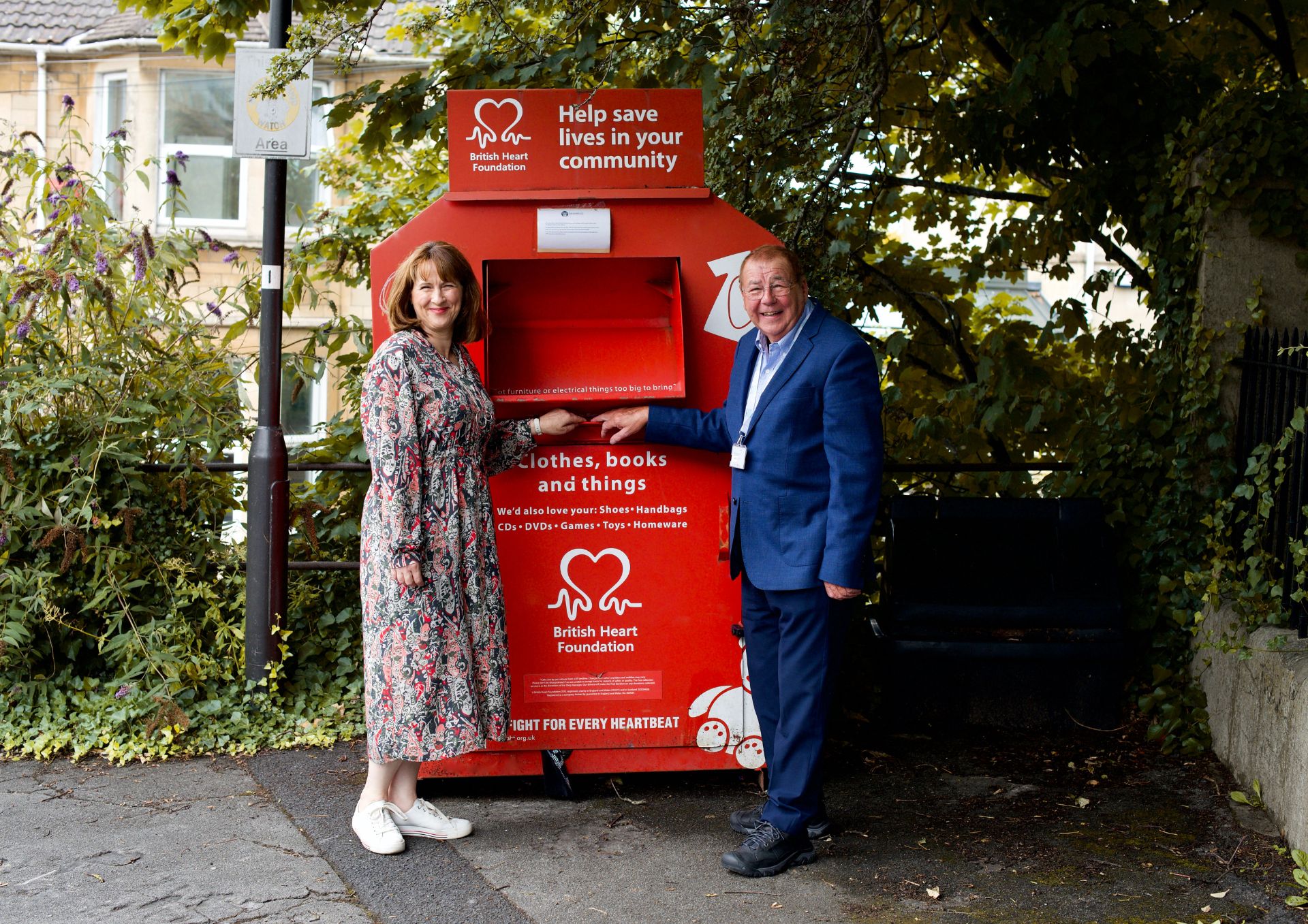 Photo of man and a woman standing next to a bright red collection box for textile