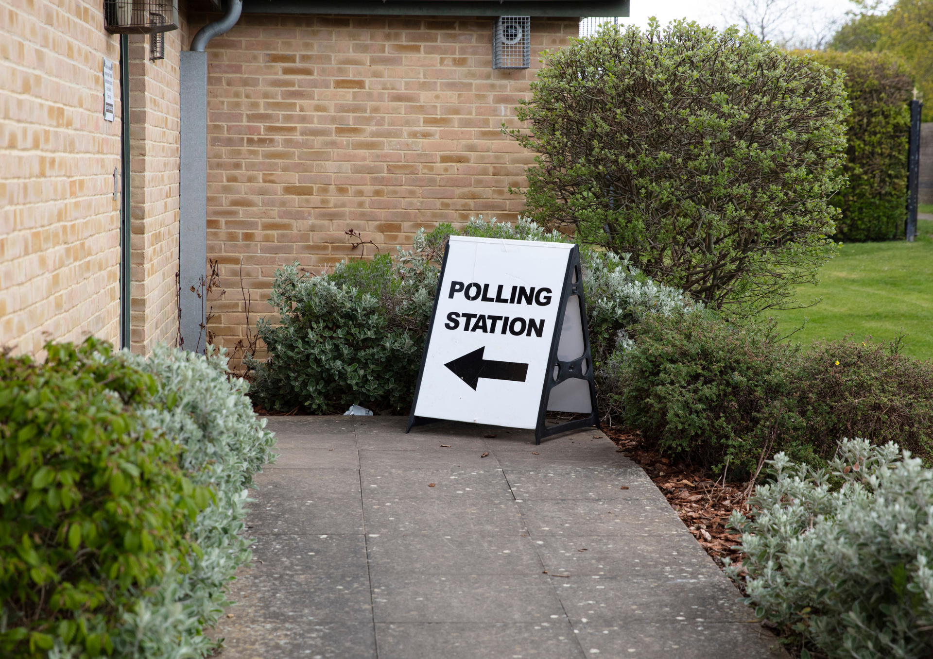 Photo of a sign saying polling station with a direction arrow on the pavement outside the entrance to a building