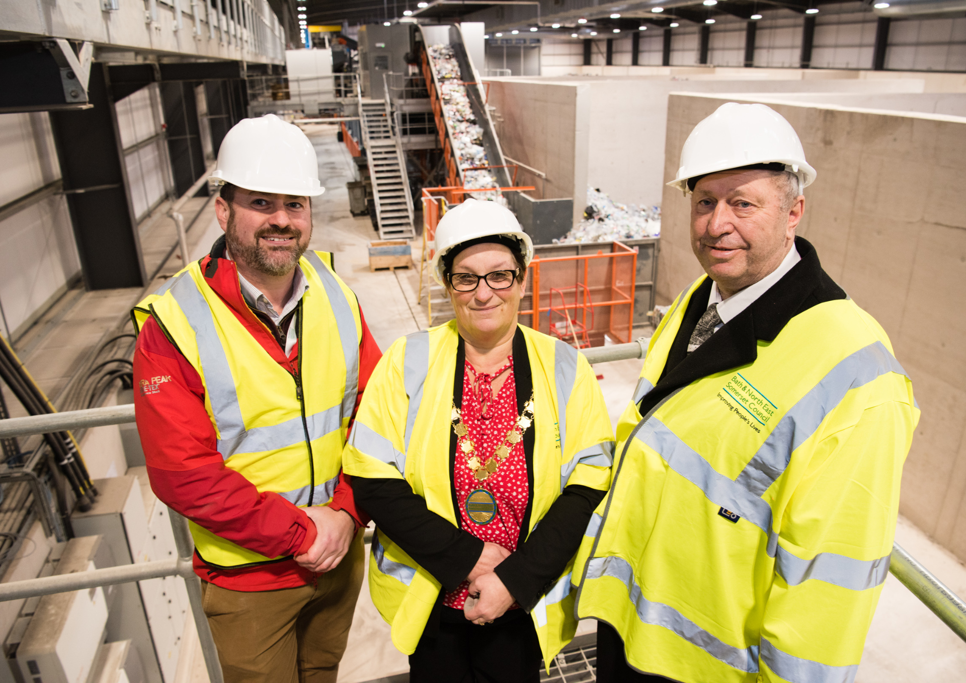 two men and a woman dress in high vis vests and hard hats inside a recycling plant