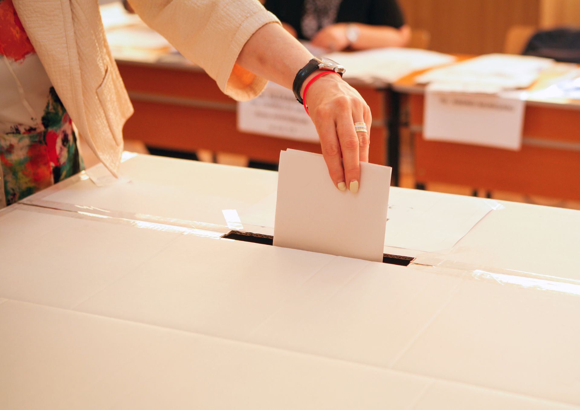 photo of a woman's hand posting a voting form into a ballot box
