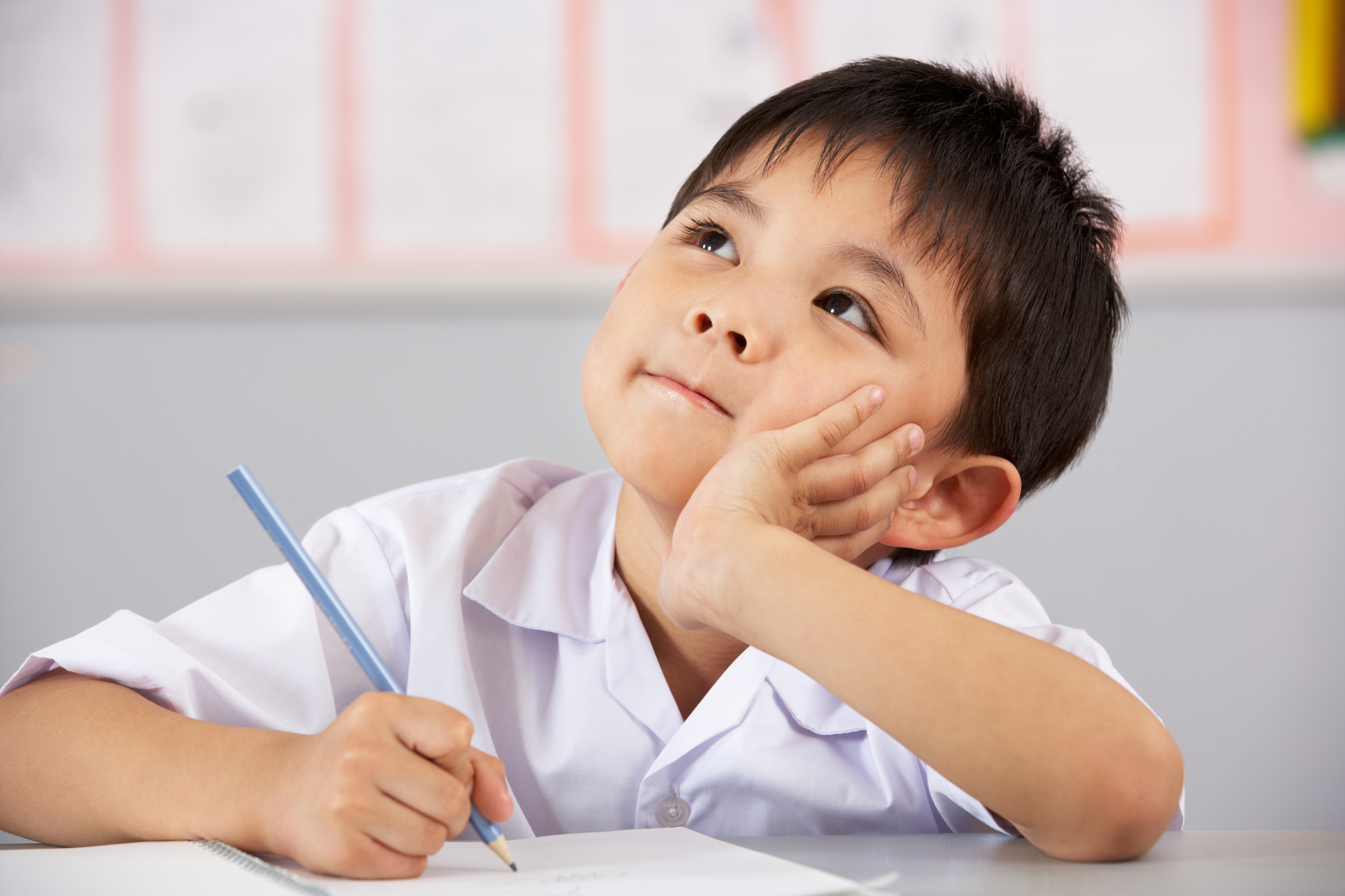 Young child sits in school at table with pencil in hand