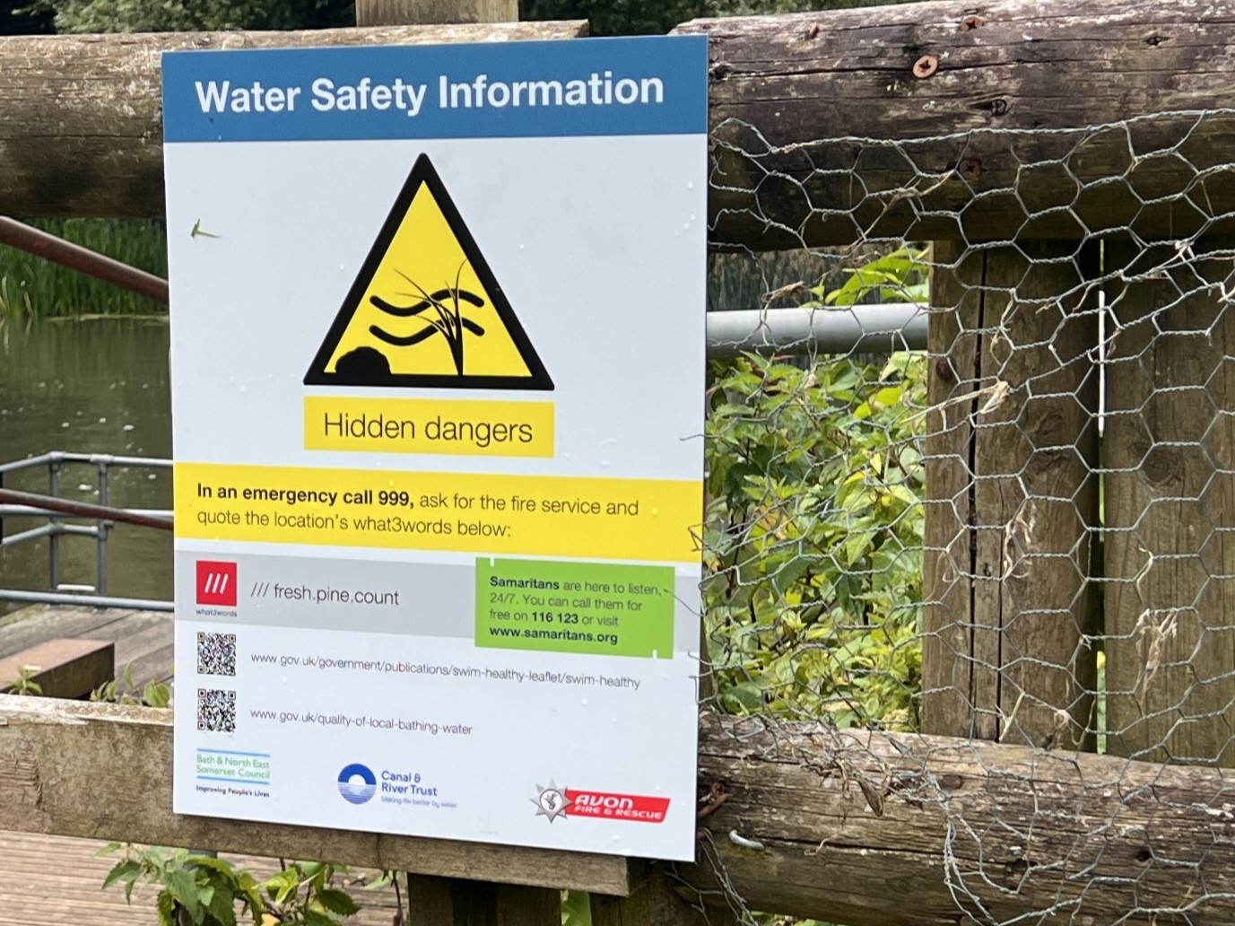 A water safety sign on a fence near open water