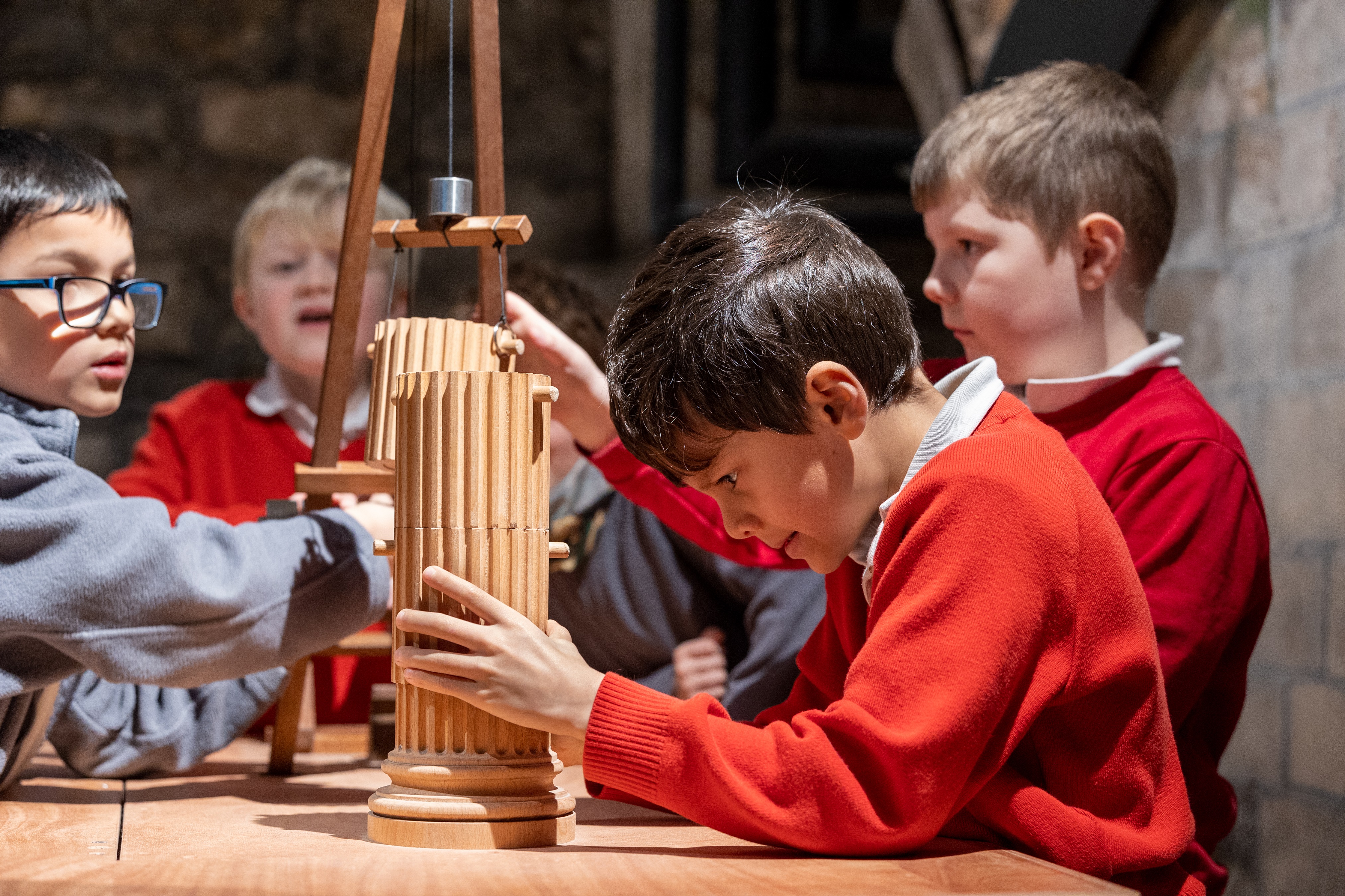 Four school boys using a model crane to construct a pillar made from wood