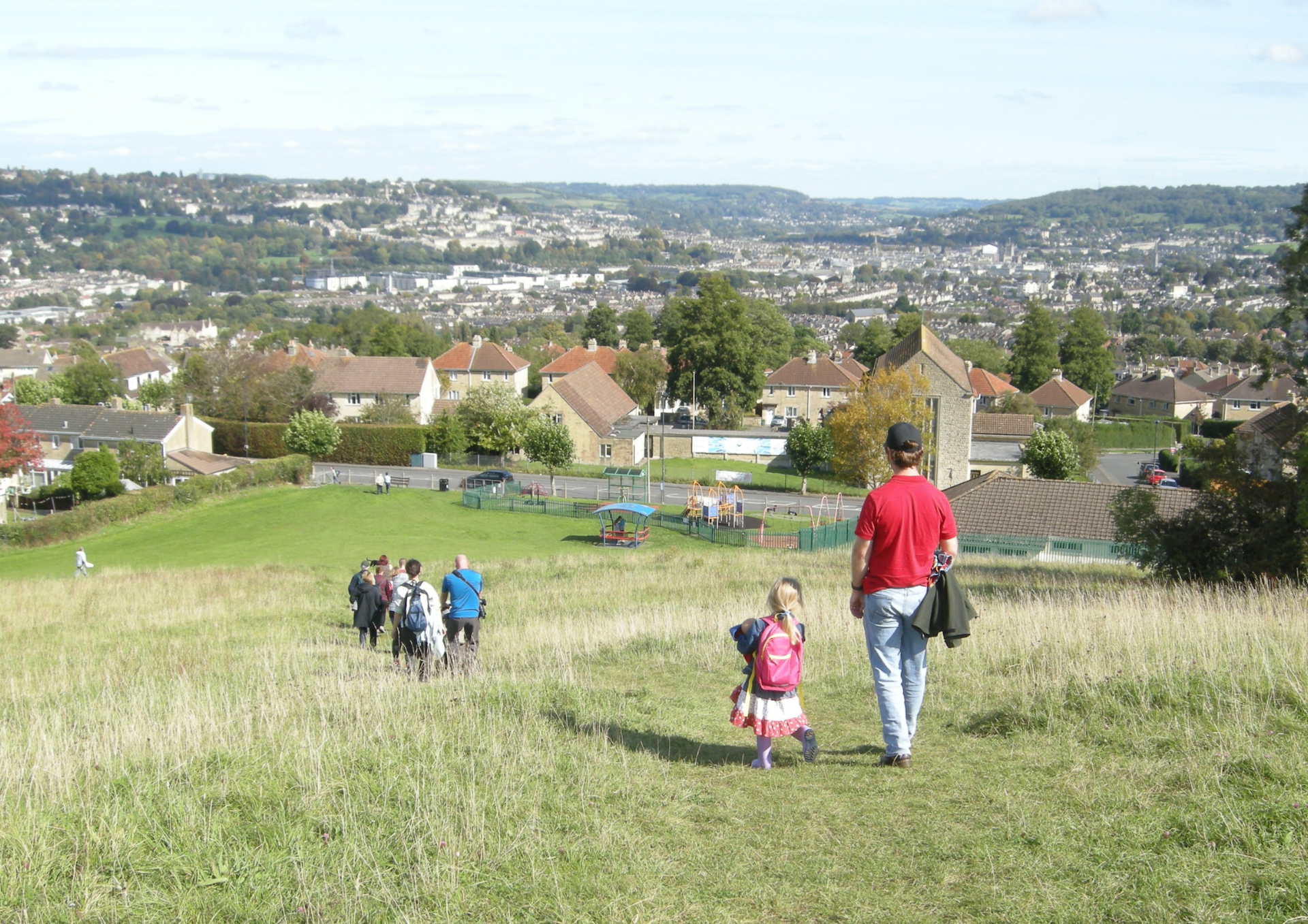 several people walking down a grassy hill. There are houses in the distance.