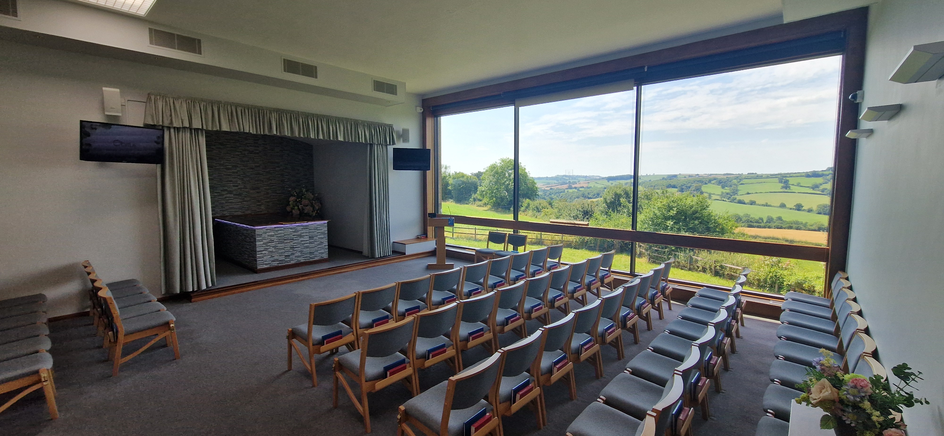 Interior of Valley Chapel at Haycombe Crematorium with chairs laid out. A view of the countryside is seen through a large window at the side of the room