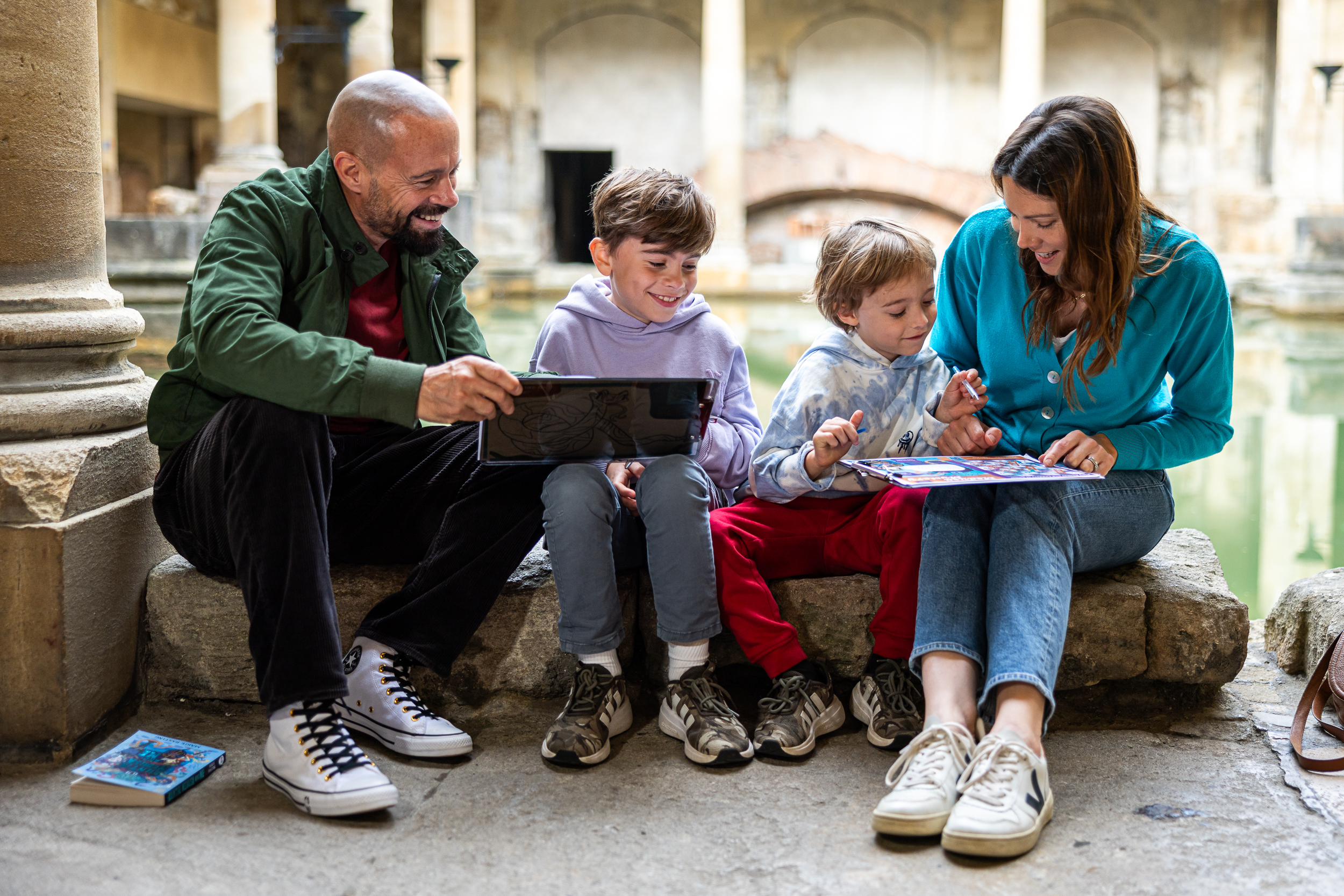 A family following a trail at The Roman Baths, sitting in front of the Great Bath