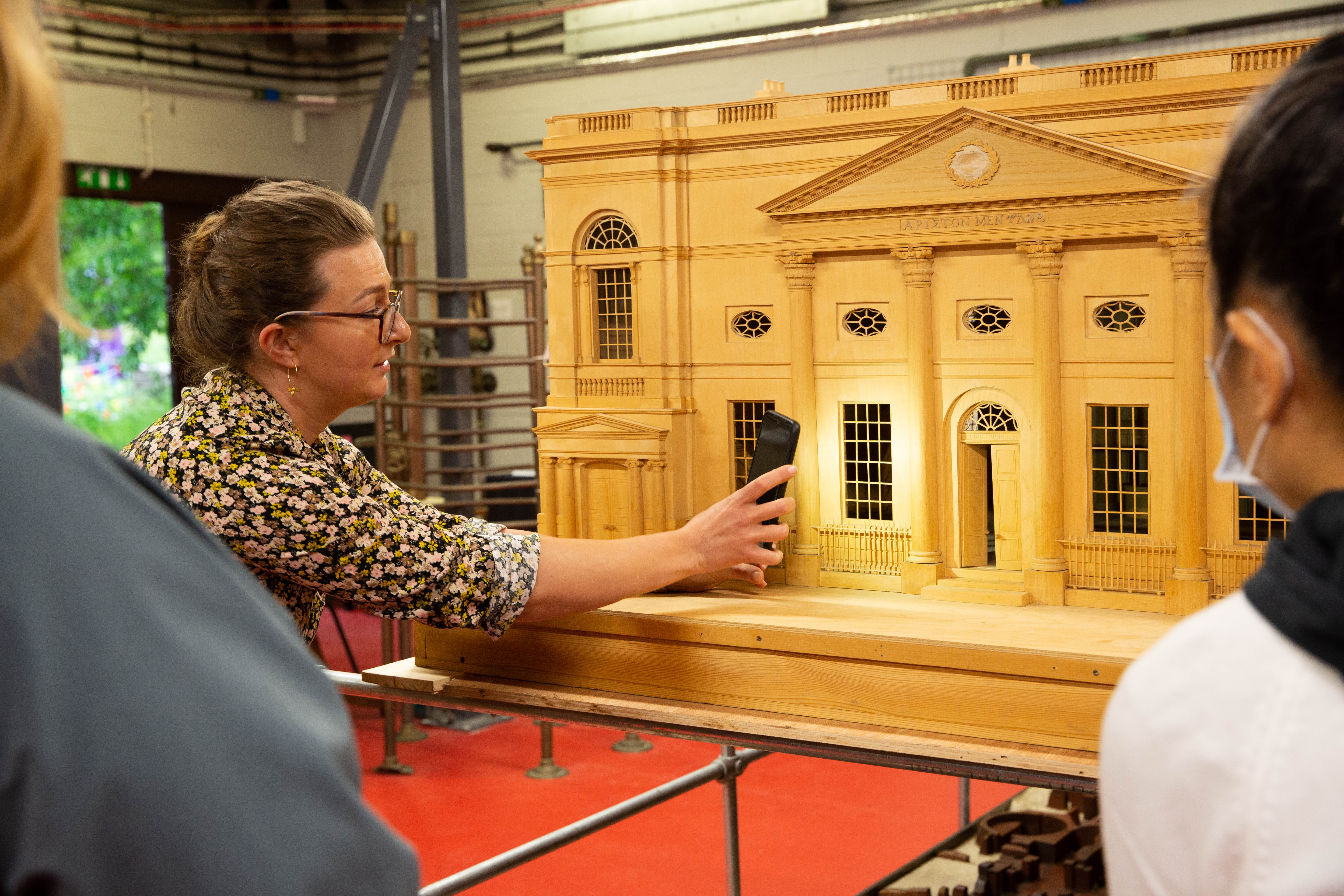 Female curator shining a phone torch into a large wooden model of a building