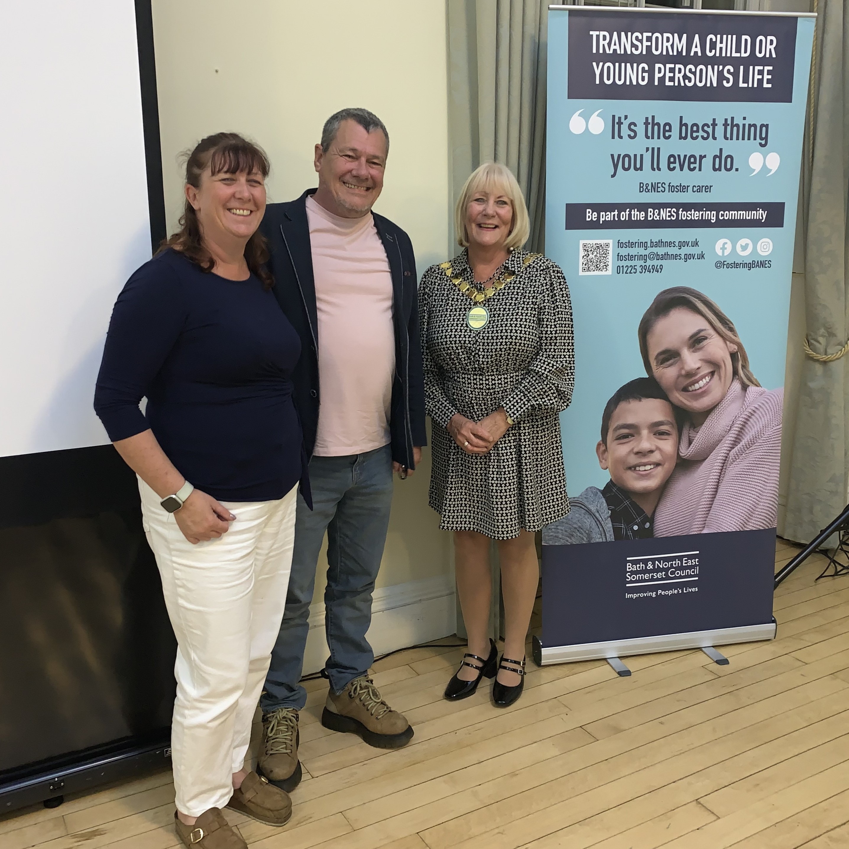 Three people stand next to a fostering pull-up banner