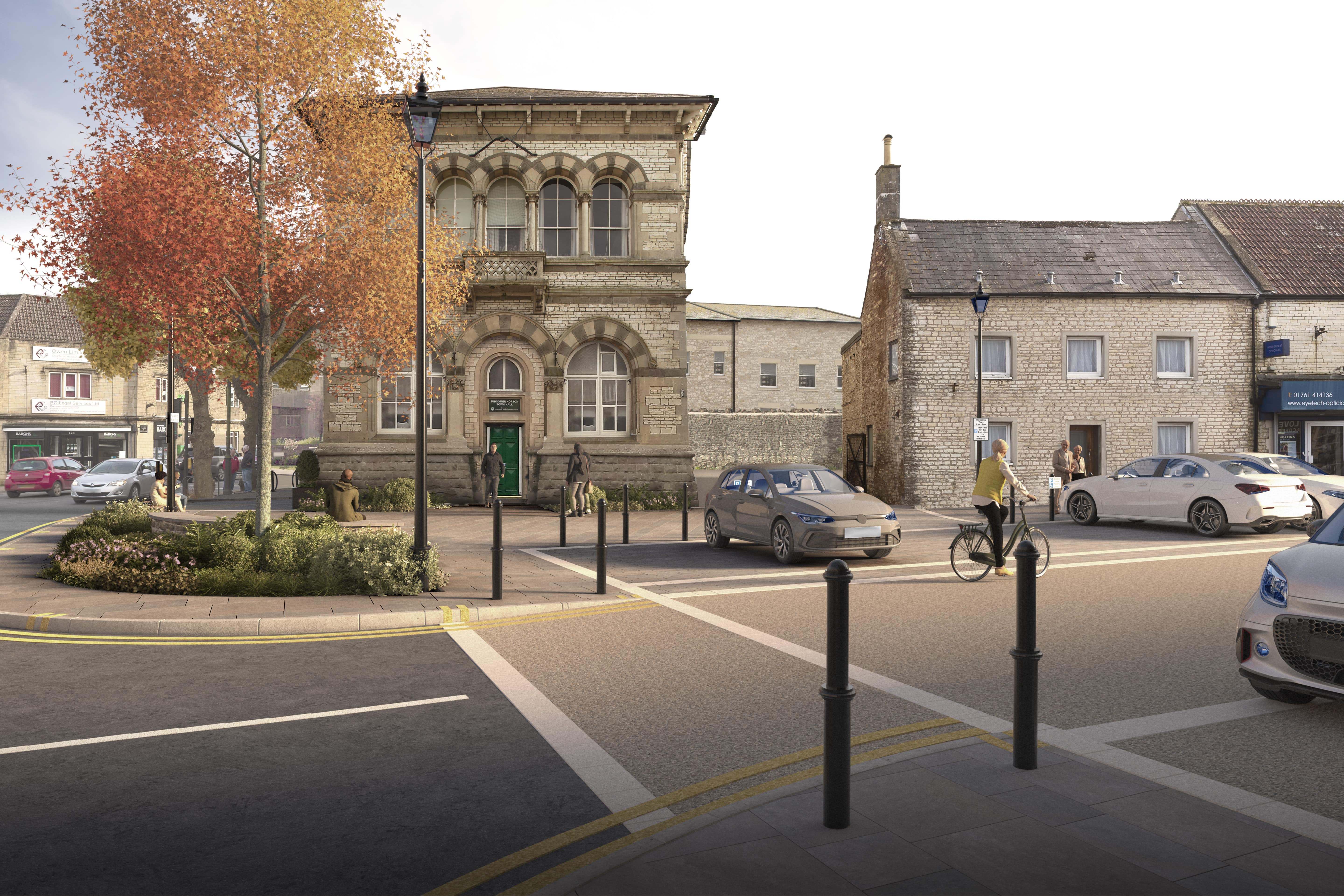 A computer-generated view of how Midsomer Norton Town Hall and the surrounding street will look once the market square project is completed. There is wider paving and a new carriageway. People sit on street furniture and stand looking at the town hall. Someone is riding a bike. There is a large tree with autumn leaf colours on the left hand side.