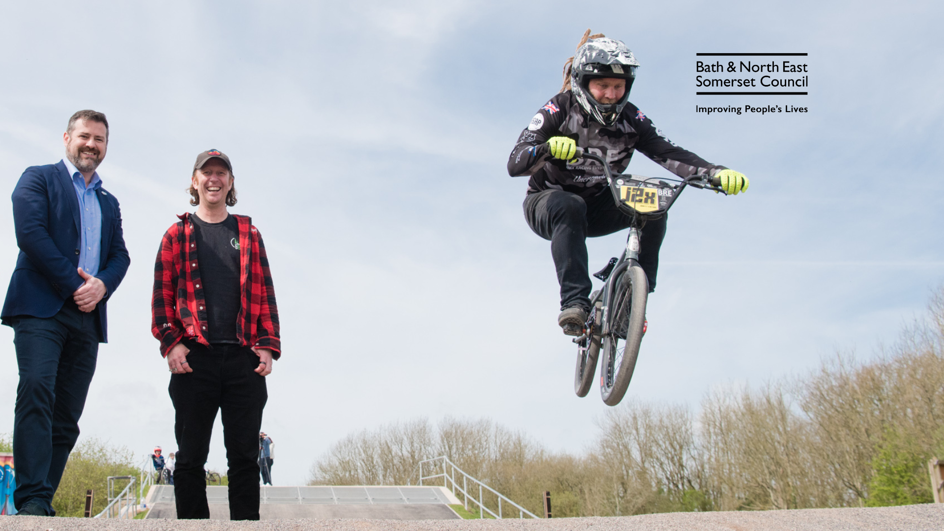 A BMX bike in the air with two people watching.