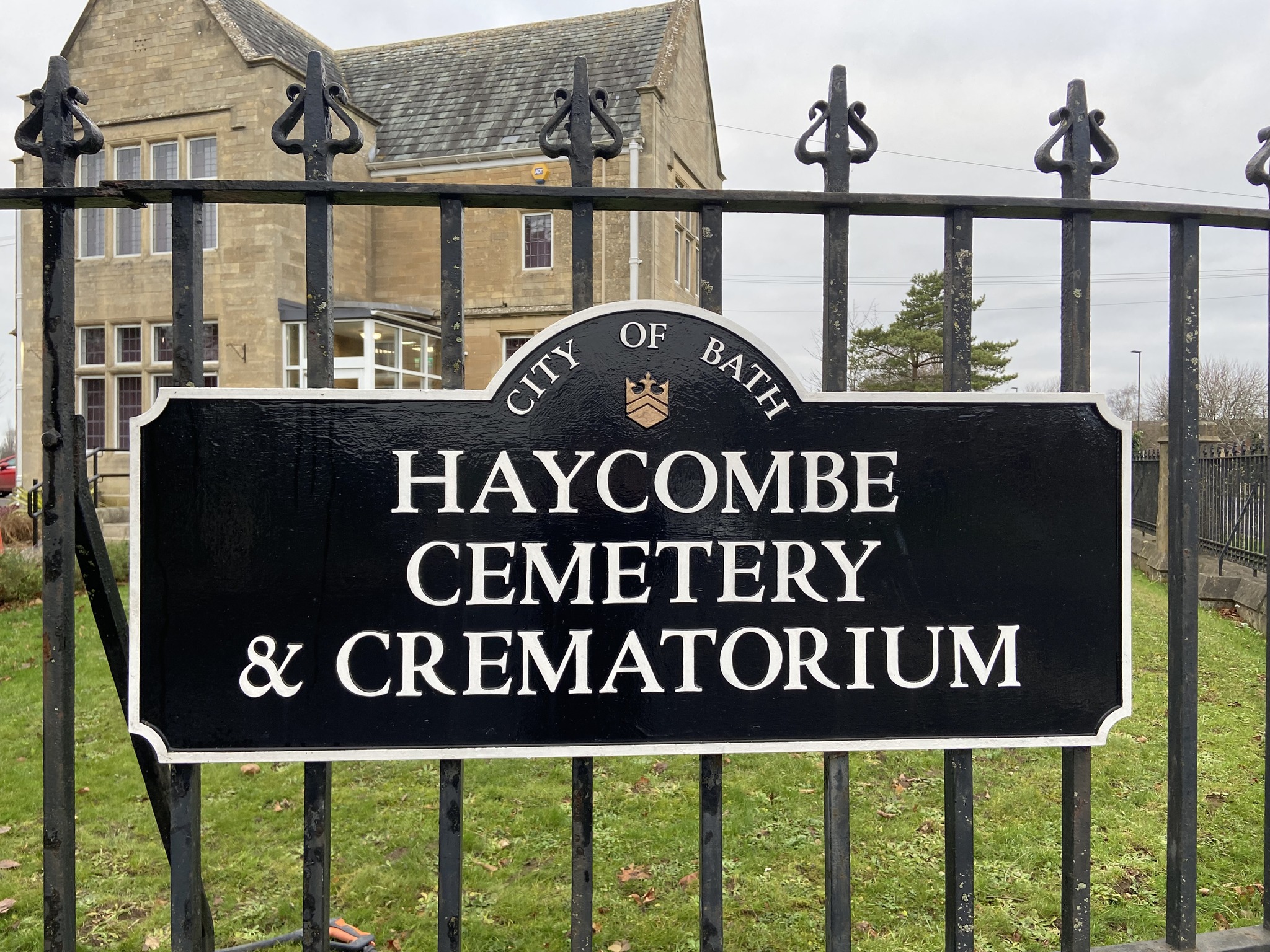 Black entrance sign with white writing on black railings at Haycombe Cemetery & Crematorium