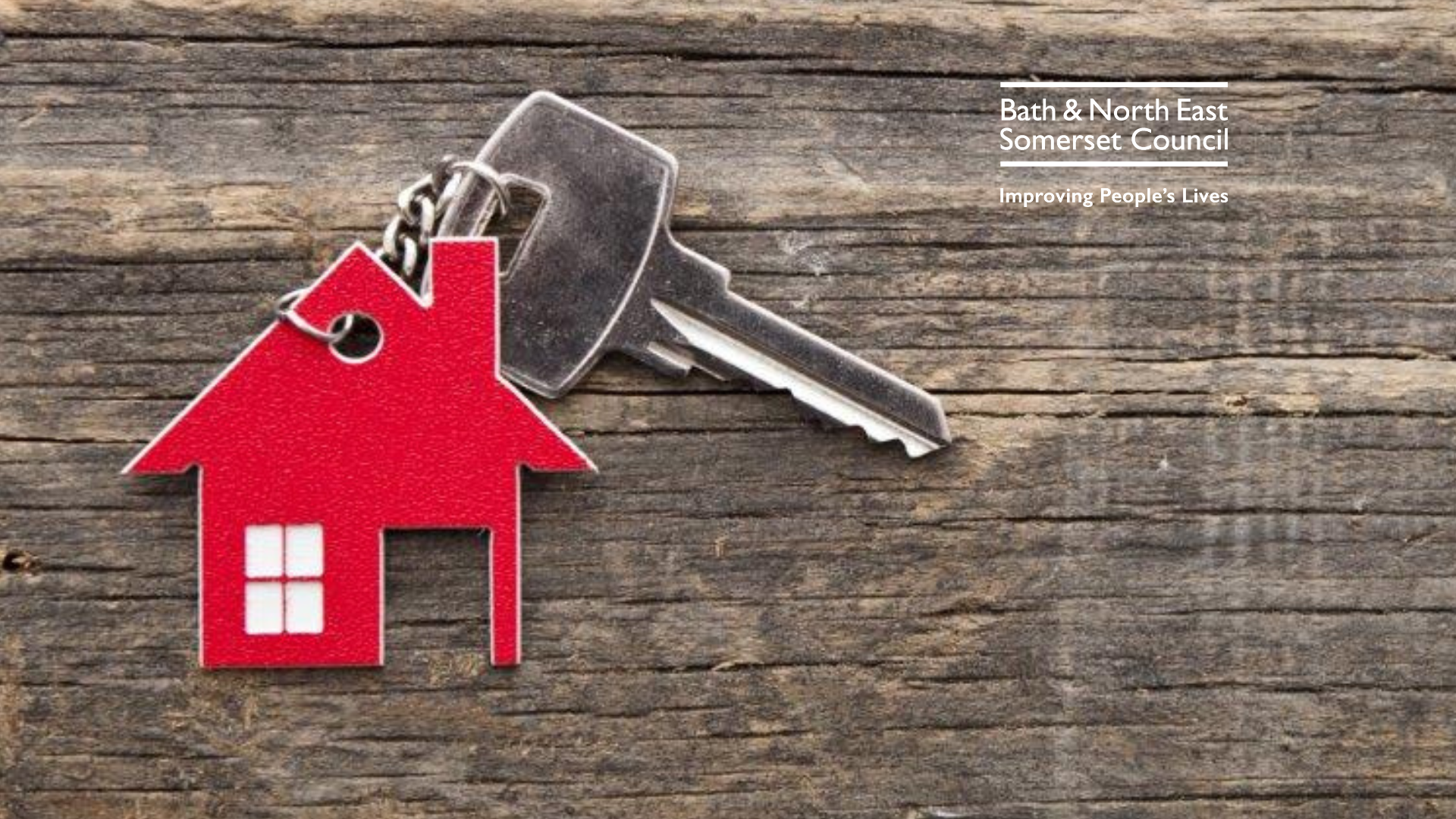 A keyring in the cut out shape of a house with a silver key attached resting on a wooden background