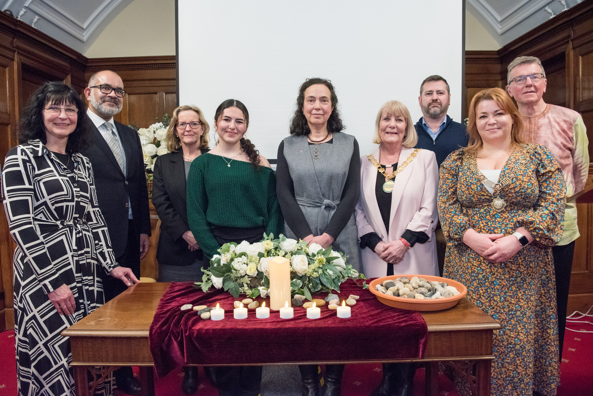 People gathered around a table on which are Holocaust Memorial Day candle tributes