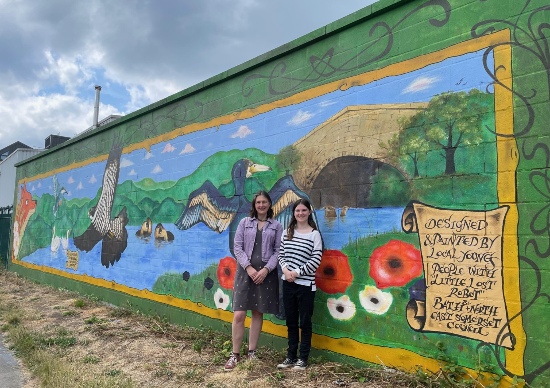 A photo of a mural on a stone wall with two women standing in front of it.