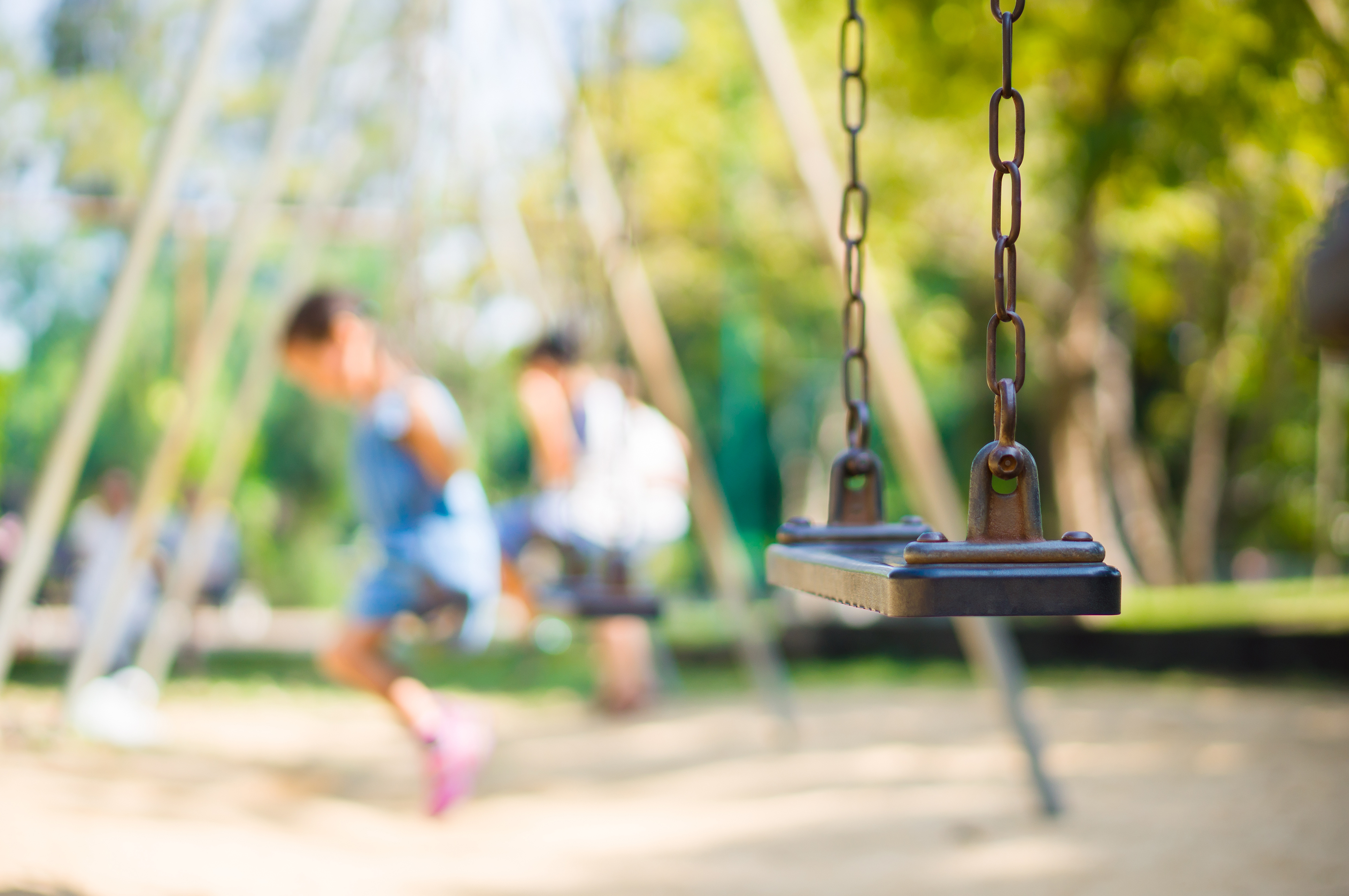 Swing in foreground with out of focus children on swings in background in a park