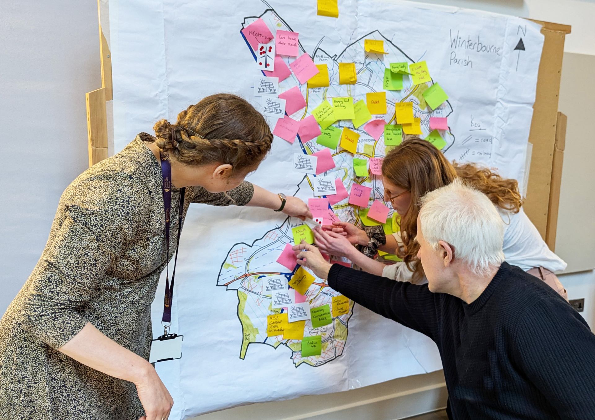 a photo of a man and two women pinning bright coloured post it notes onto a map