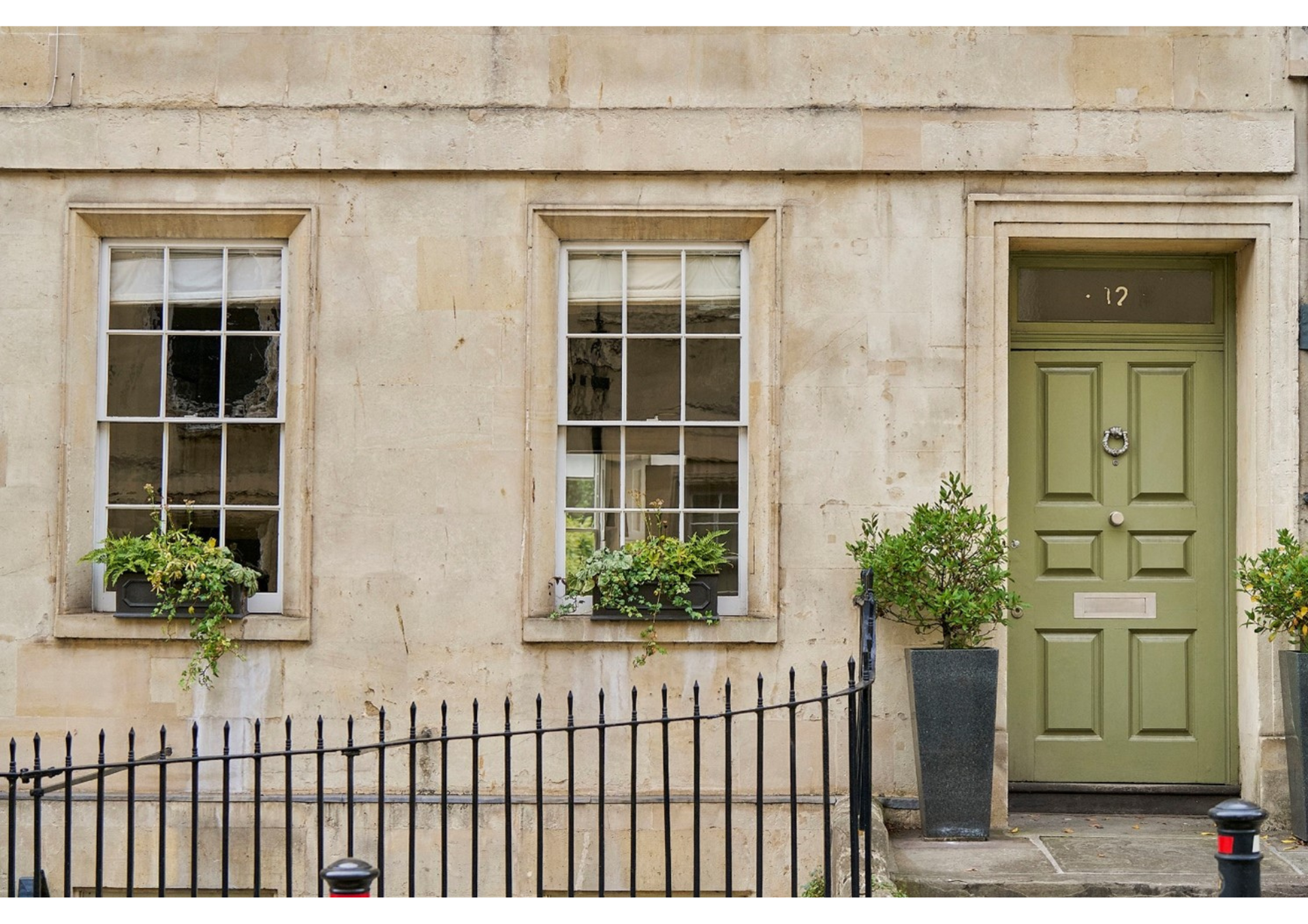 a photo of the outside of a Georgian house with sash windows and a green front door with black railings outside