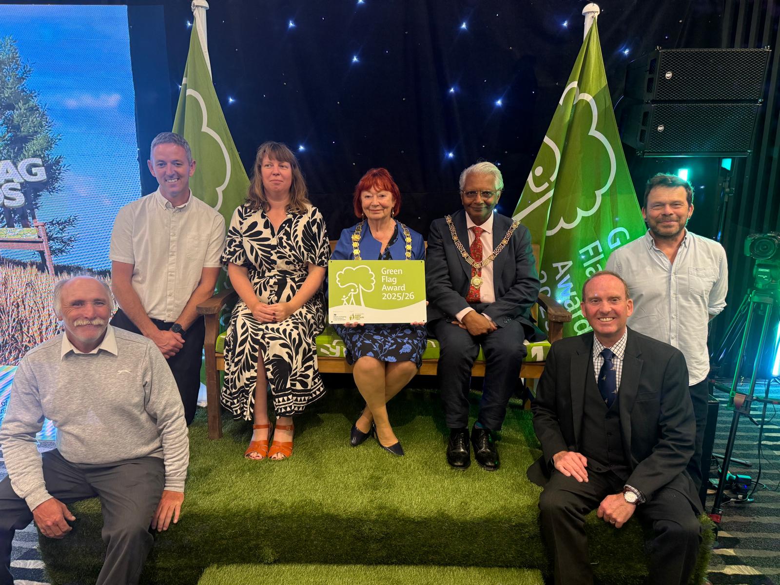 A group of people with the person in the middle holding up a Green Flag Award banner