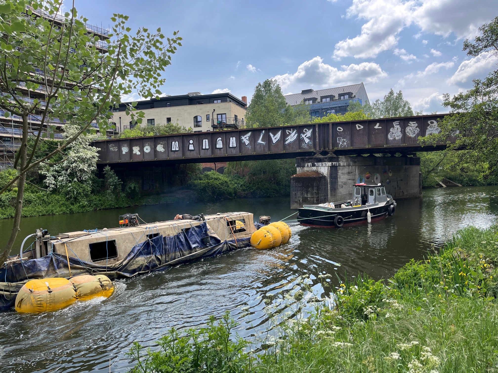 Sunken boat being removed from river by a towboat