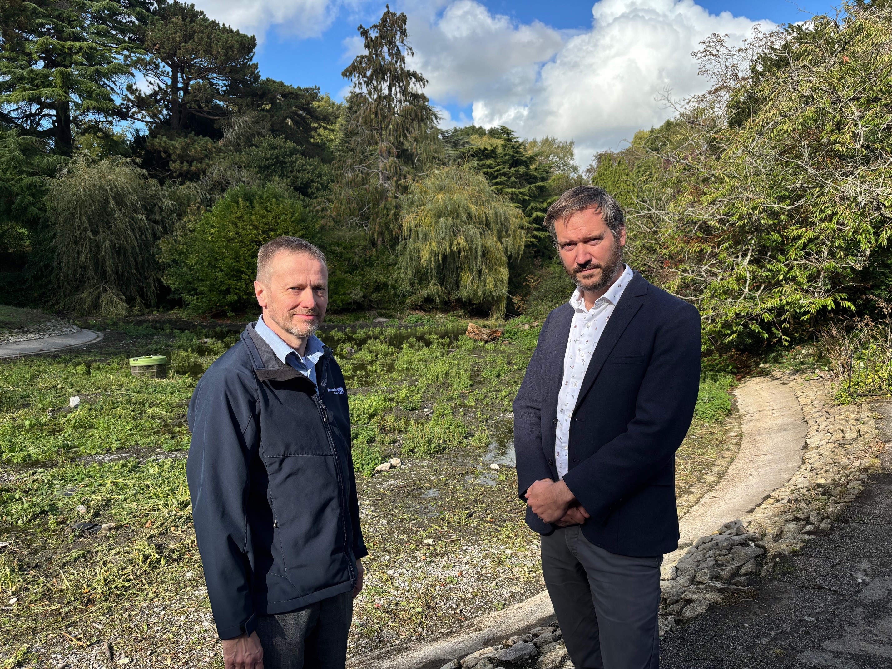 Two people stand in front of a dried-up pond