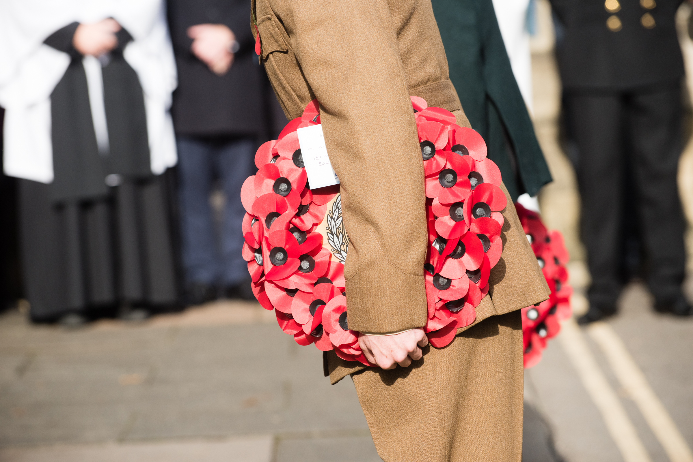 Person in uniform holds poppy wreaths at their sides