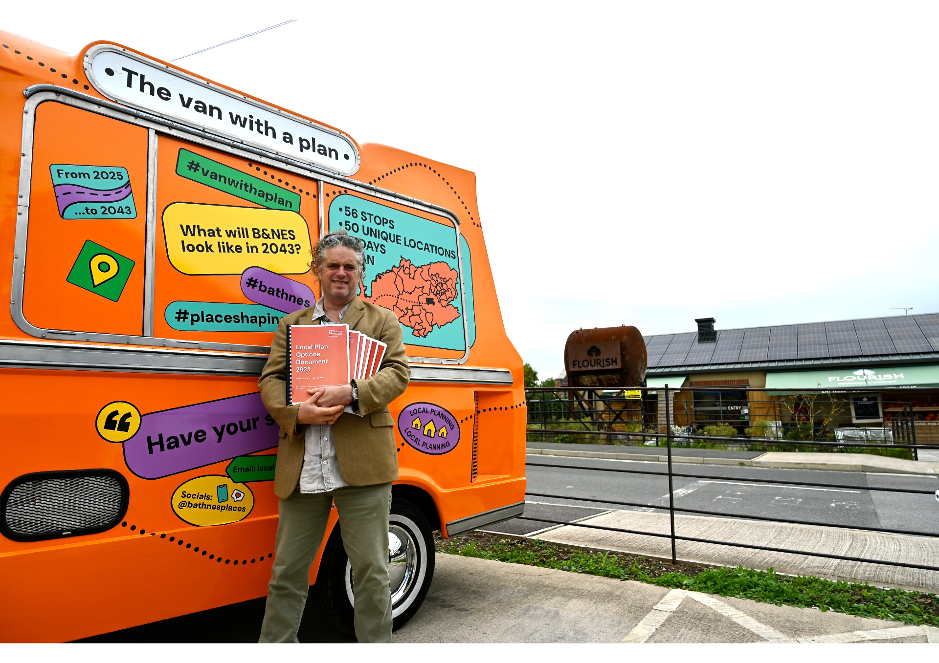 an orange van decorated with stickers about the local plan and a sign on the top saying van with a plan. A man leaning against the van holding a bundle of A4 leaflets. A building in the background.