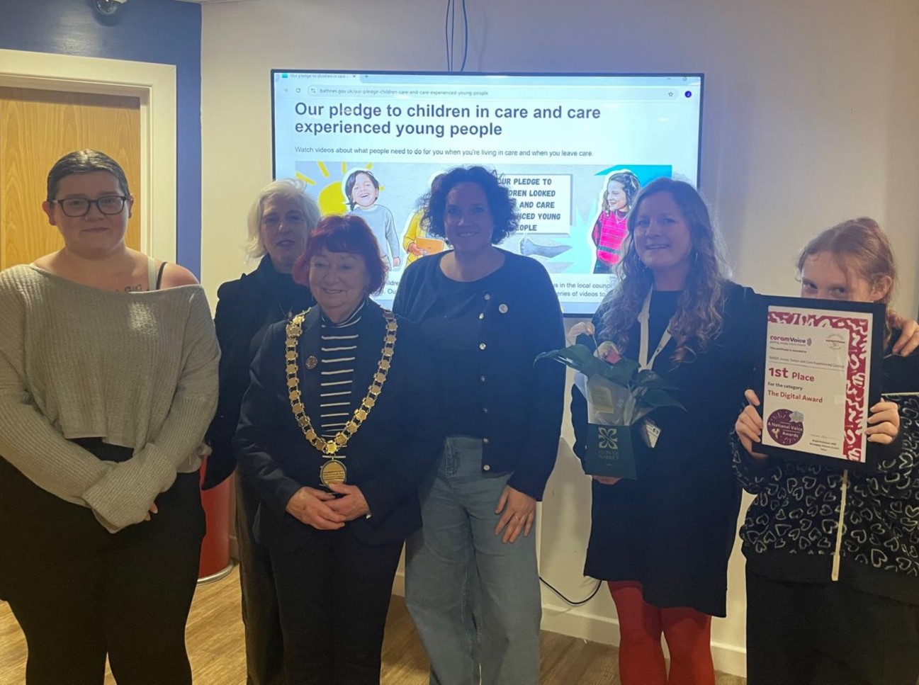 a group of 6 people stand in front of a whiteboard screen, one holds an award 