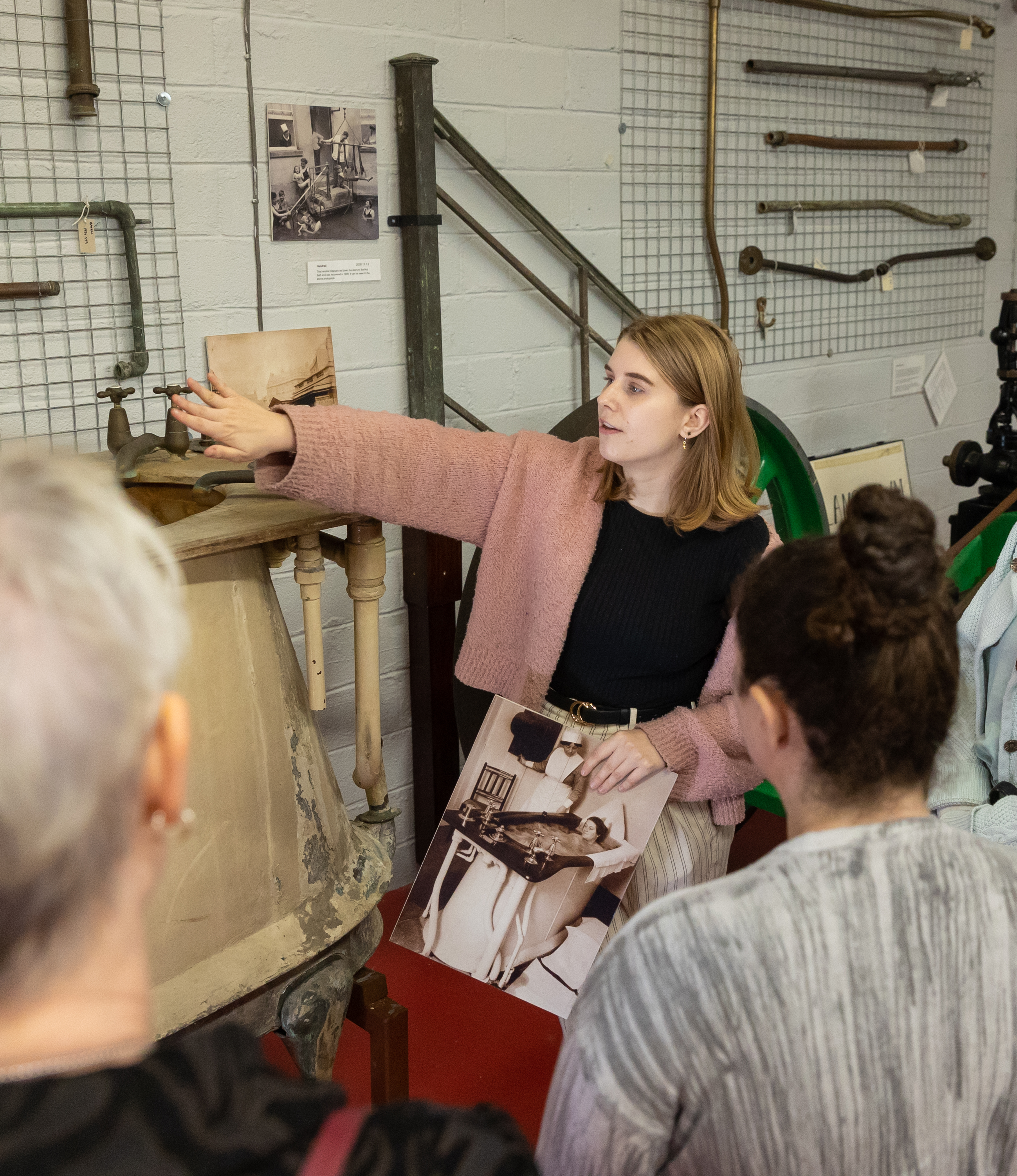 A young female curator shows historic spa equipment to two tour attendees