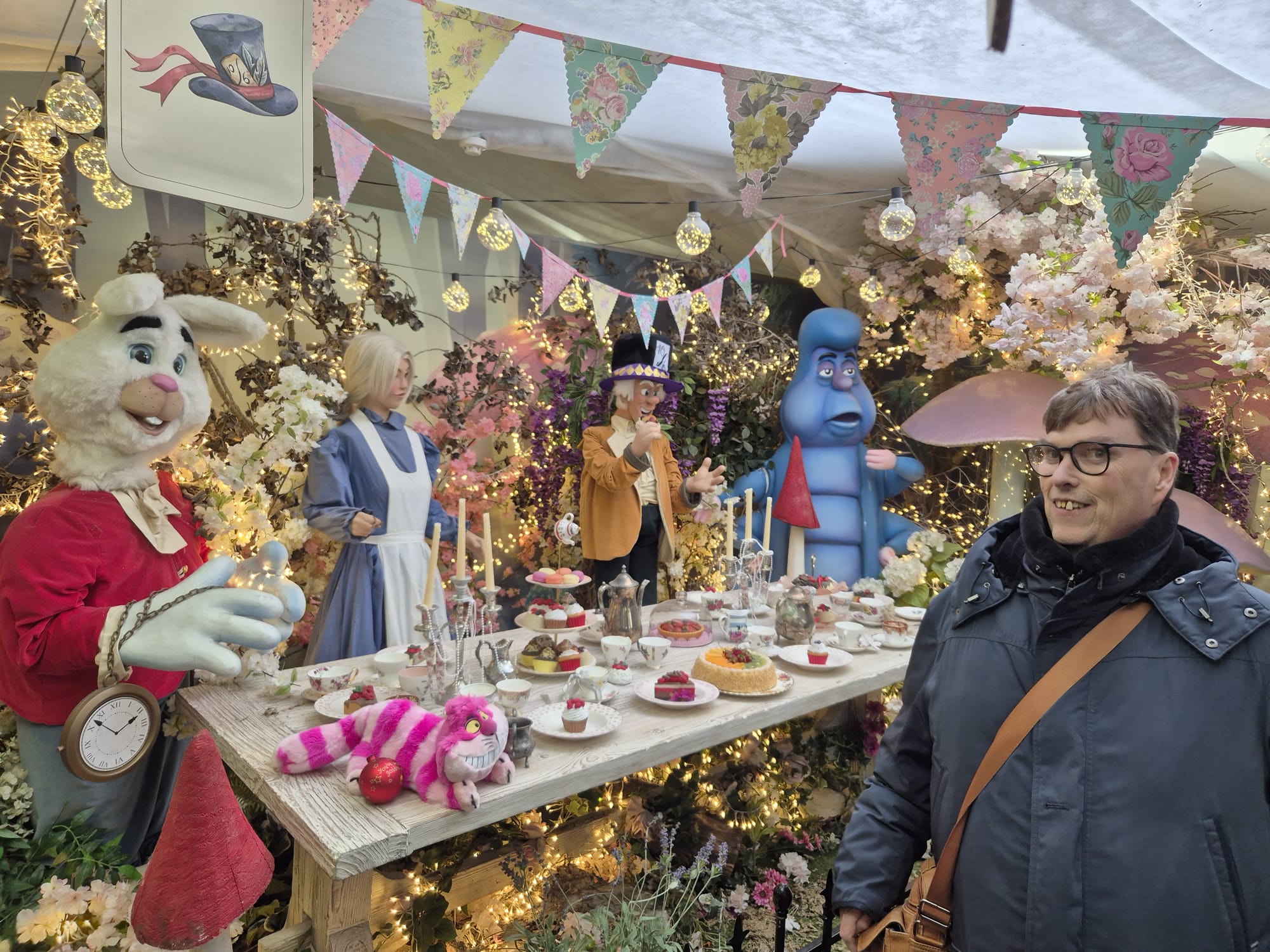 Shared Lives user R stands in front of an Alice in Wonderland themed display at Lacock Abbey National Trust, with support from Carer, Sue