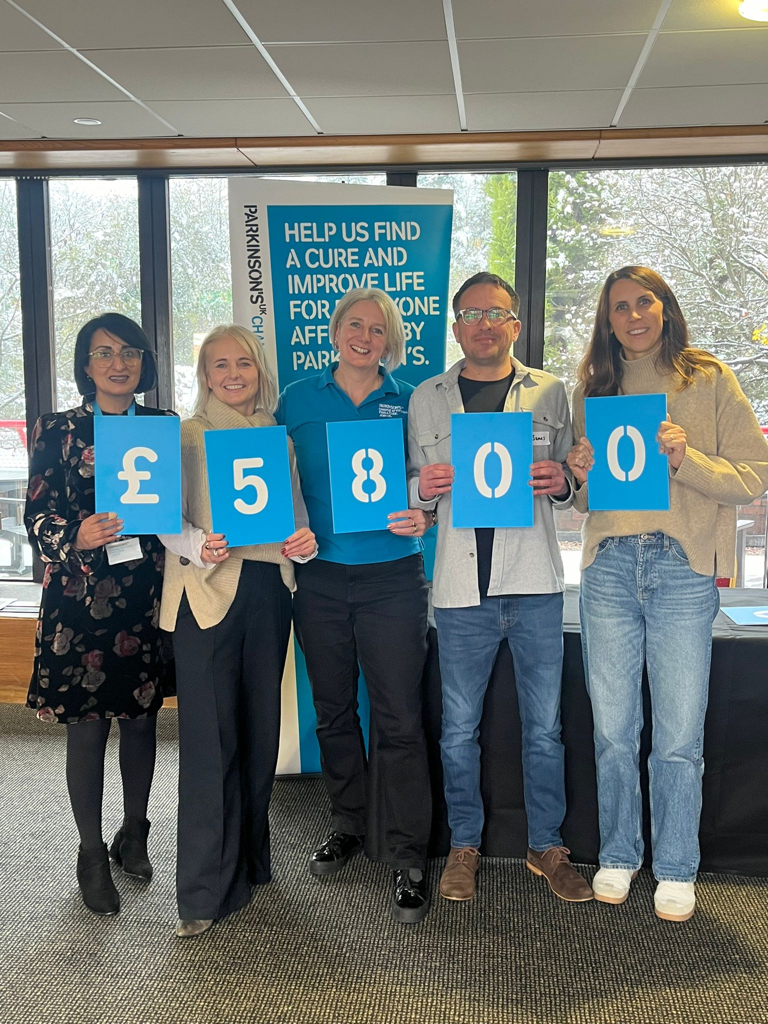 Five people hold up blue numbers to form £5800