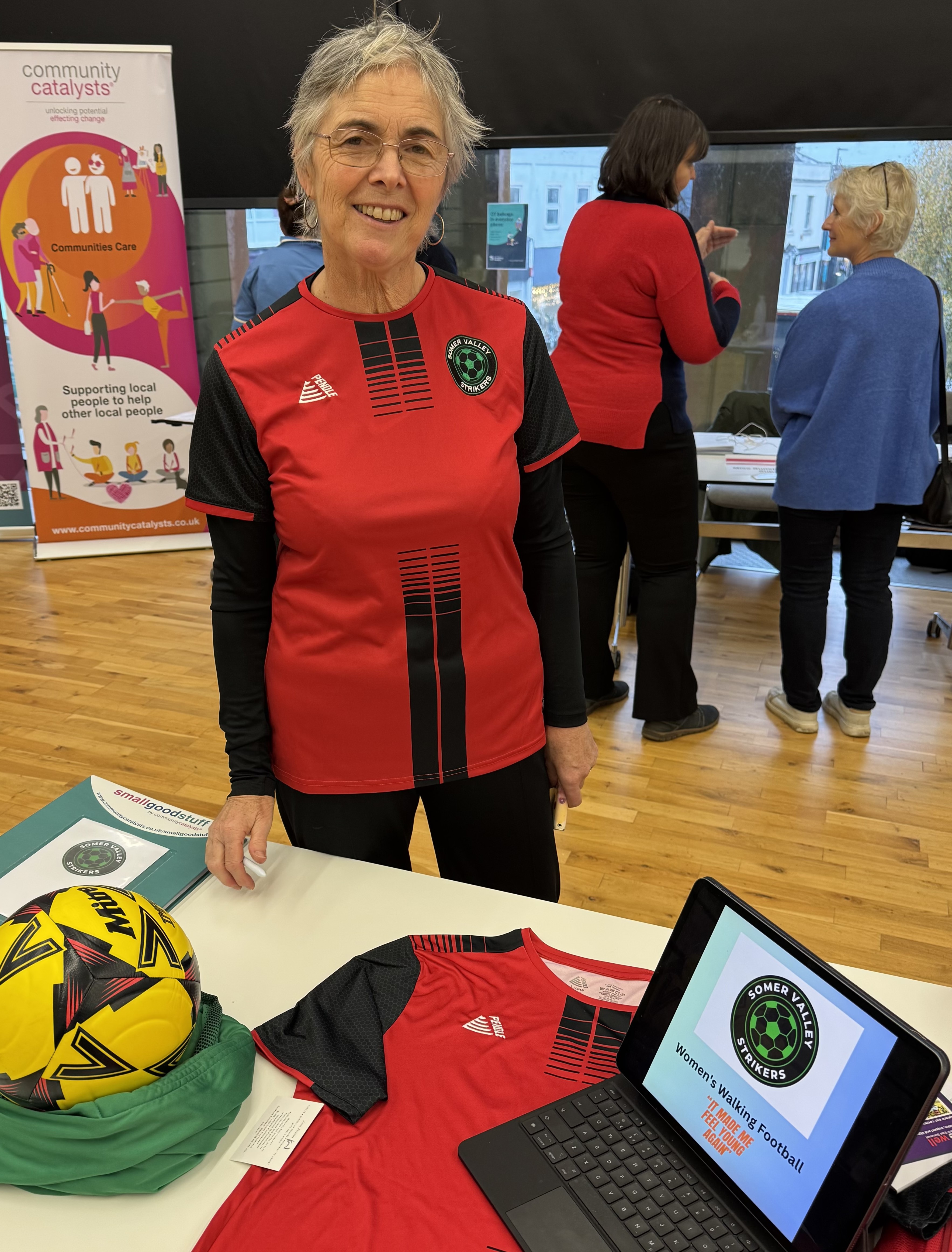 Amanda Bachrach, manager of Somer Valley Strikers walking football club, standing at their table at the Community Catalyst event